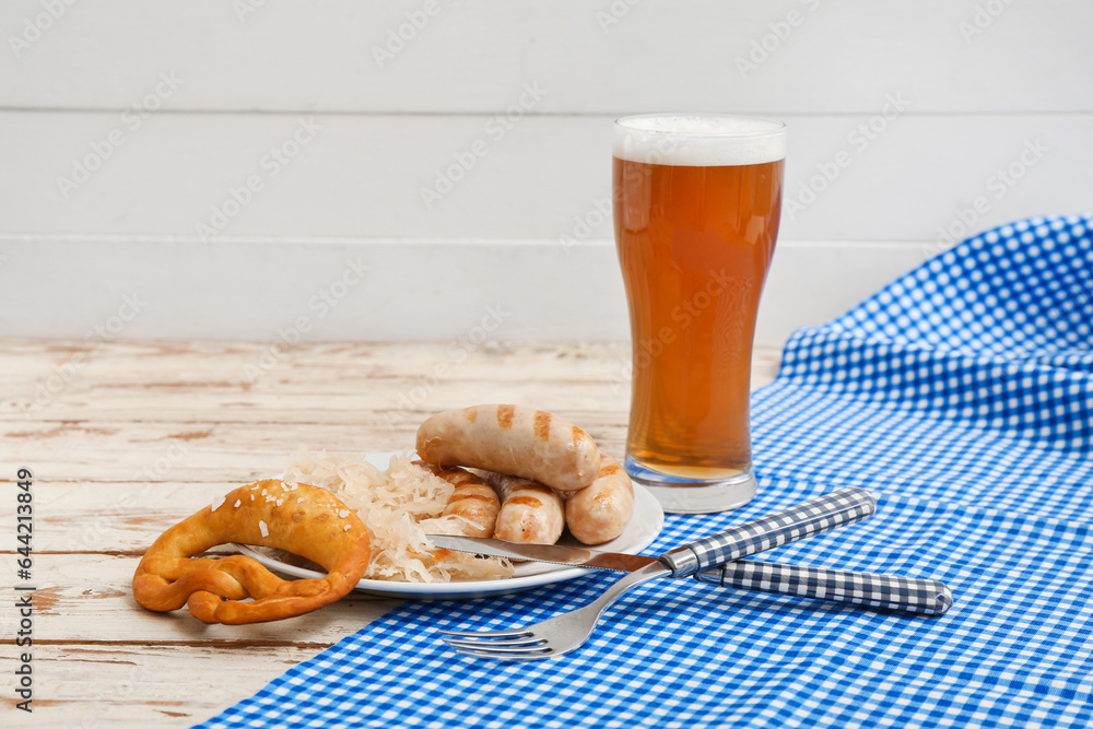 Plate with tasty Bavarian sausages, pretzel, sauerkraut and glass of beer on white wooden background