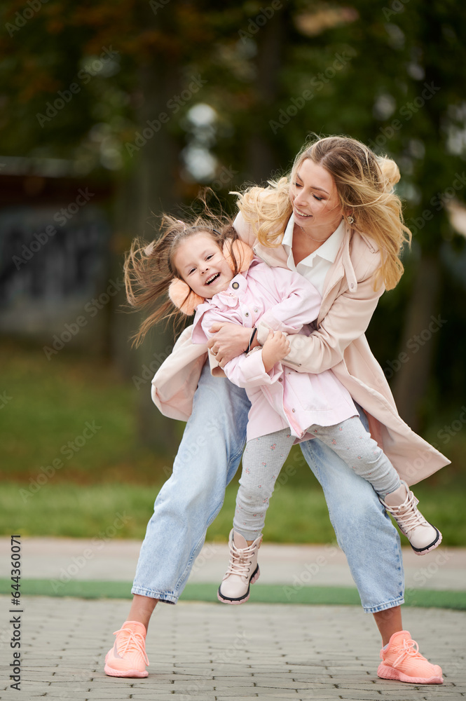 Full length of cheerful woman holding little girl and smiling while standing on the street against b