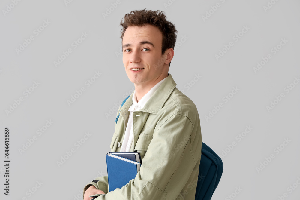 Male student with backpack and books on grey background