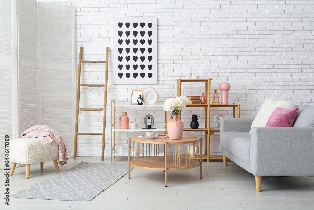 Vase of white peonies on coffee table, couch and shelving unit near white brick wall