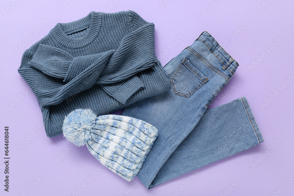 Stylish childrens sweater, jeans and warm hat on lilac background