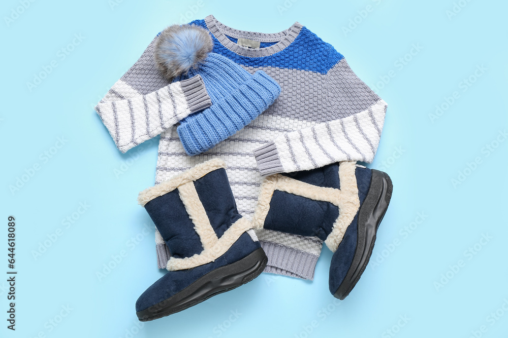 Stylish childrens sweater, shoes and warm hat on color background