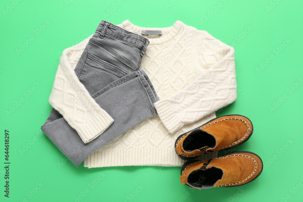 Stylish childrens sweater, jeans and boots on green background