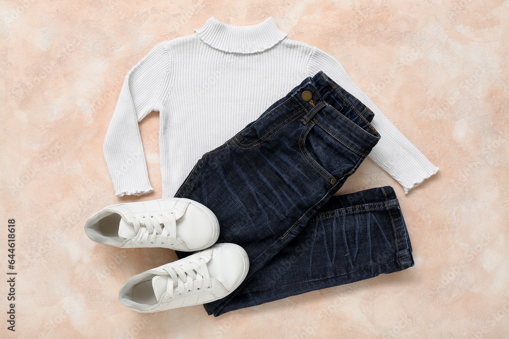 Stylish childrens sweater, jeans and shoes on color background