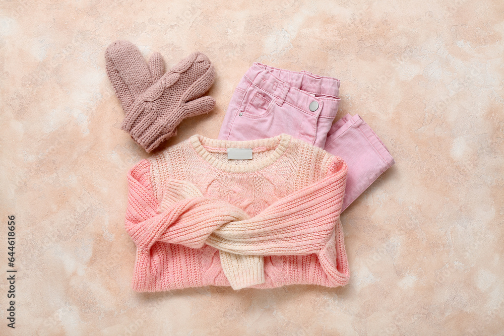 Knitted childrens sweater, pants and mittens on color background