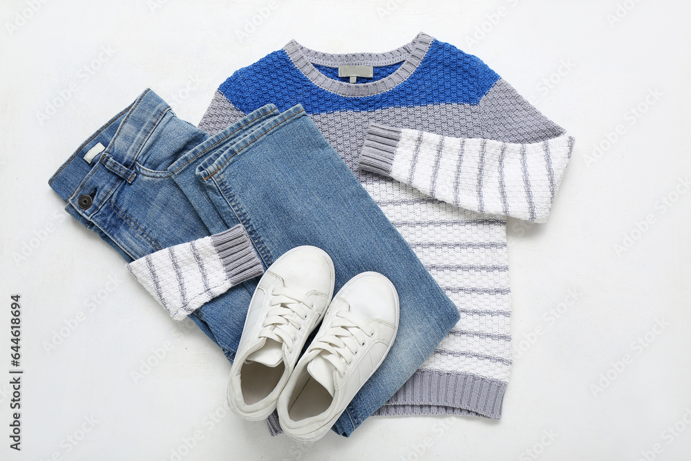 Stylish childrens sweater, jeans and shoes on light background