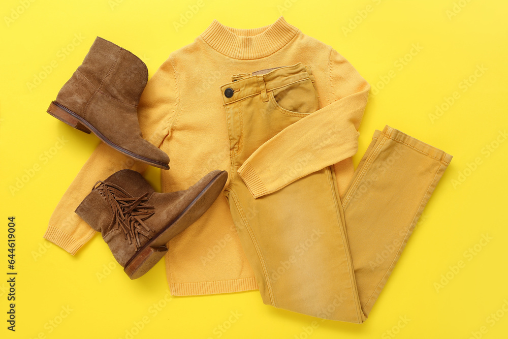 Stylish childrens sweater, pants and shoes on yellow background