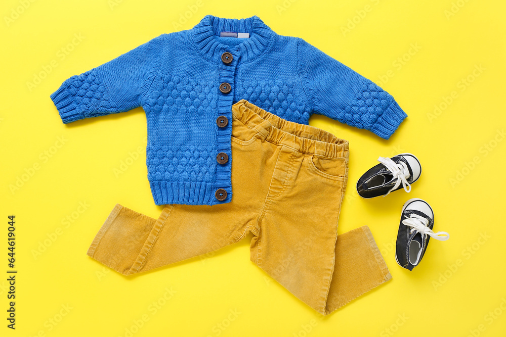 Stylish baby sweater, pants and booties on yellow background