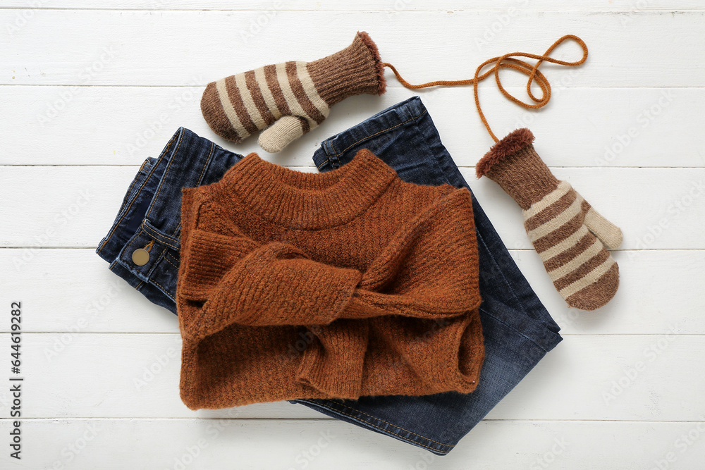 Stylish childrens sweater, jeans and warm mittens on light wooden background