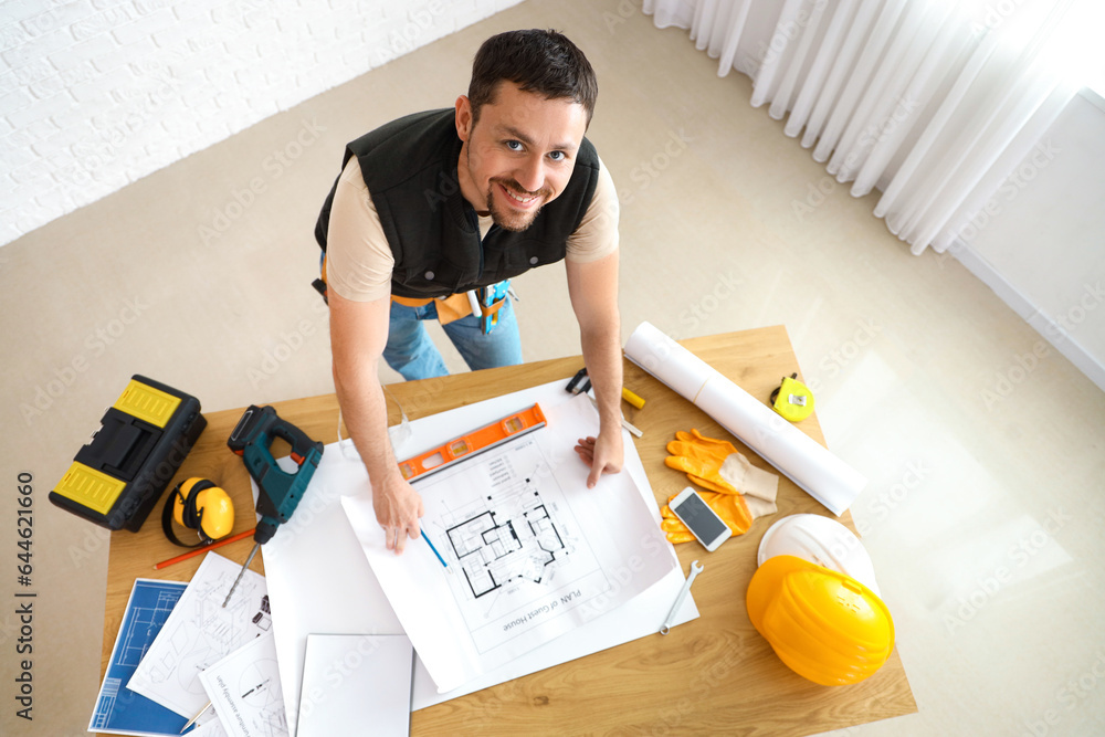 Male builder working with house plan at table in room, top view