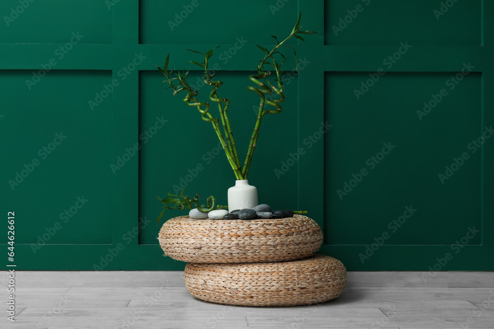 Vase with bamboo stems and stones on pouf against color background