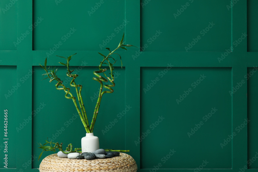 Vase with bamboo stems and stones on pouf against color background