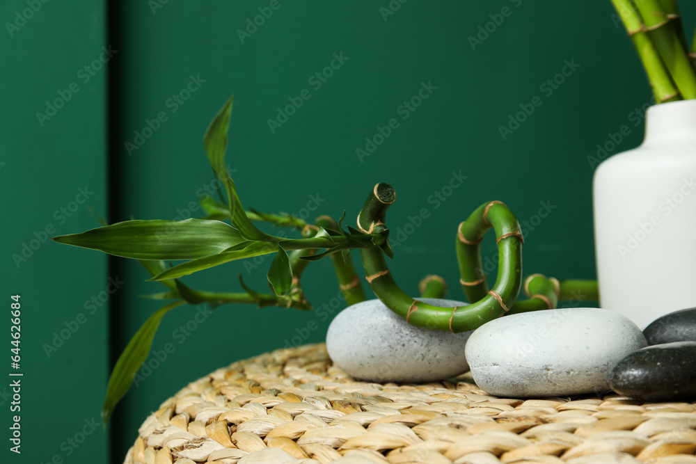 Vase with bamboo stems and stones on pouf against color background, closeup