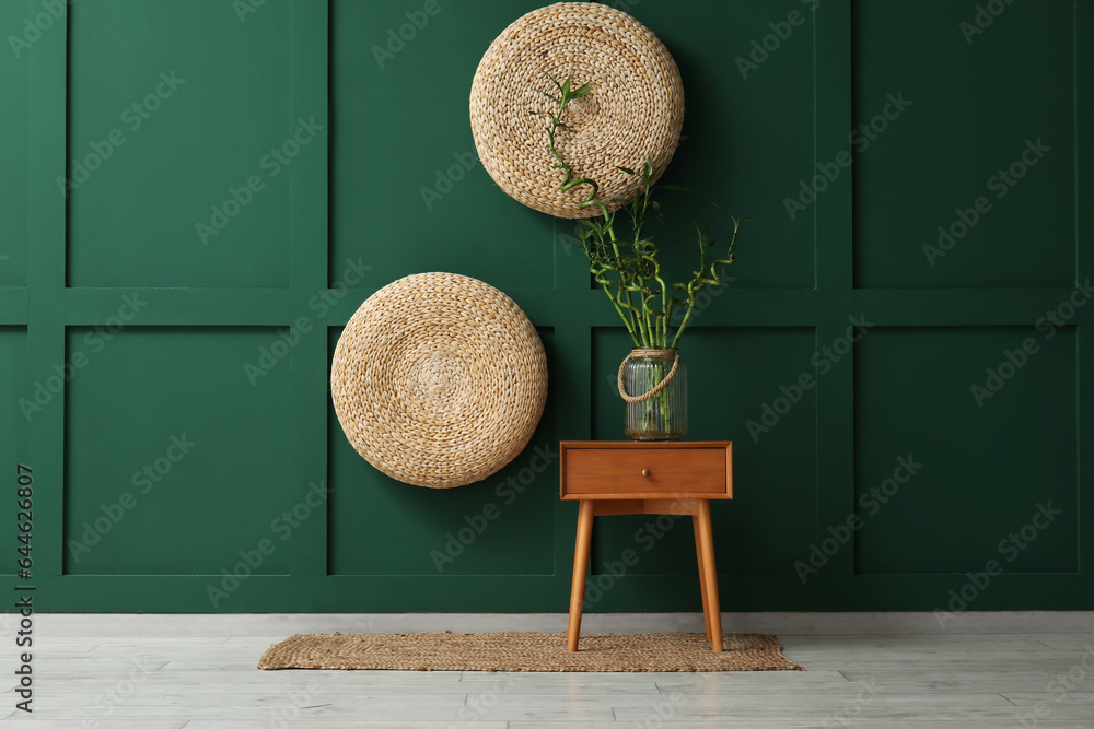 Vase with bamboo stems on wooden table near color wall