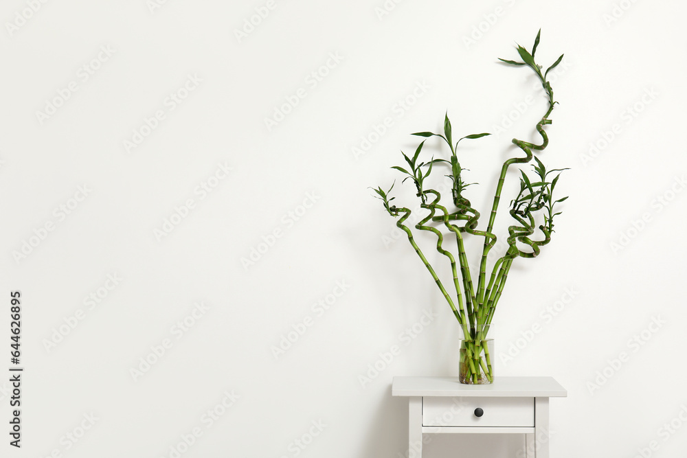 Vase with bamboo stems on table near light wall