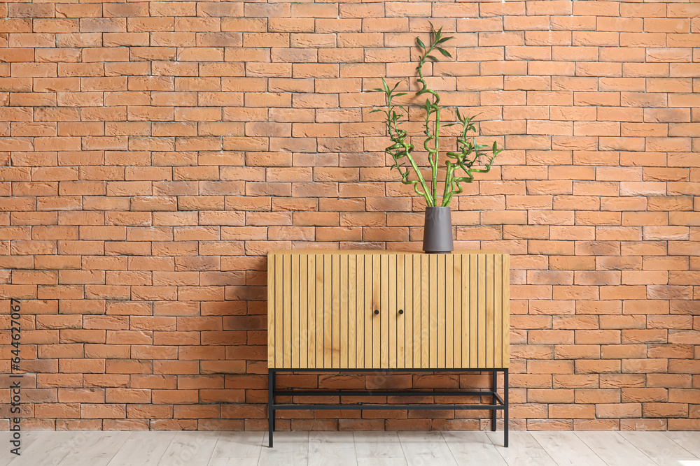 Vase with bamboo stems on table near brick wall