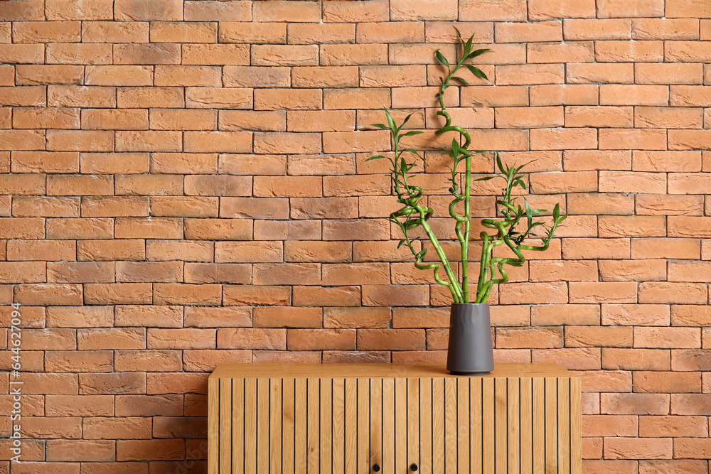 Vase with bamboo stems on table near brick wall