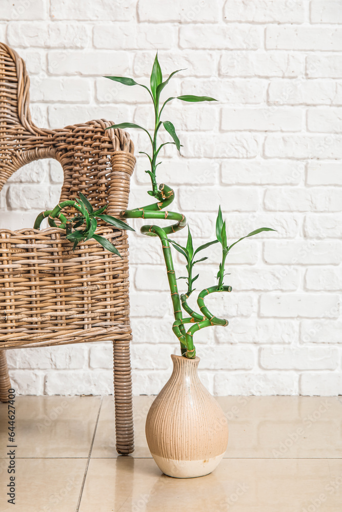 Vase with bamboo stems and rattan armchair near brick wall