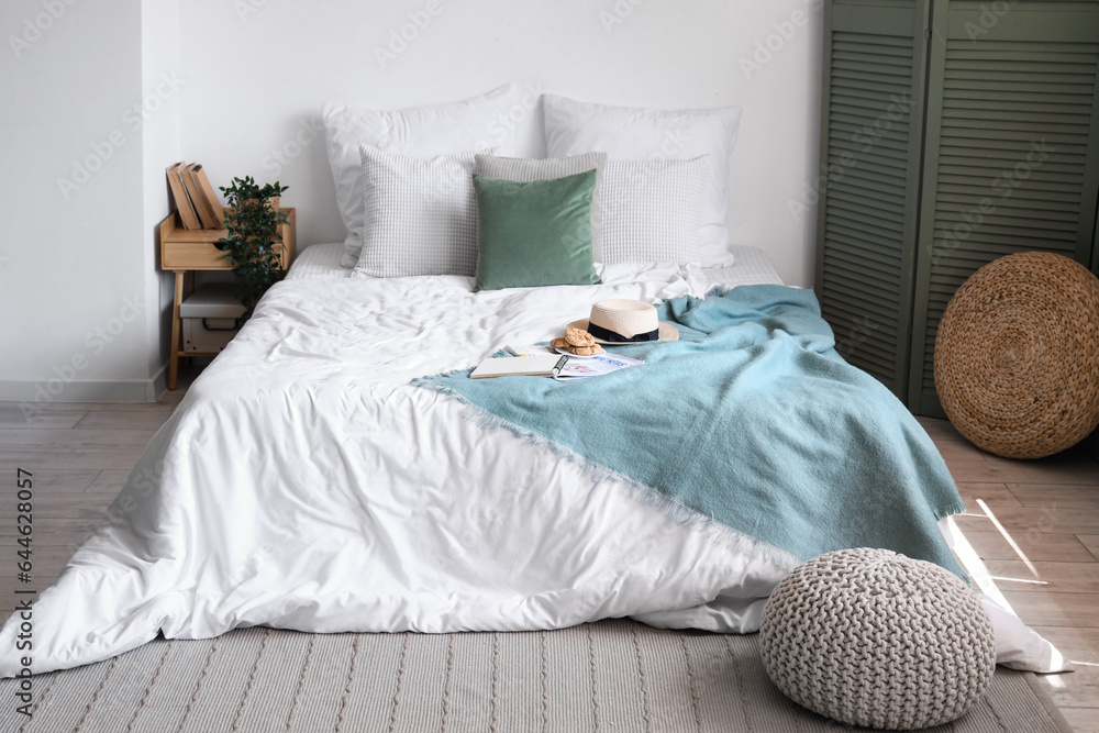 Cozy bed with white blanket, hat and cookies in stylish bedroom