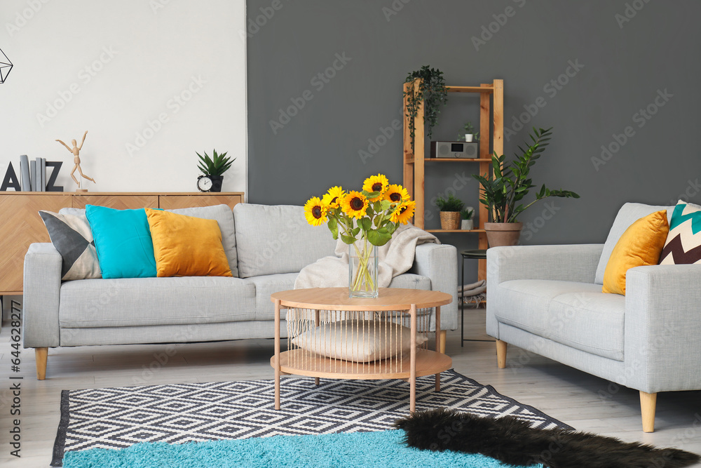 Cozy grey sofas and vase with beautiful sunflowers in interior of light living room