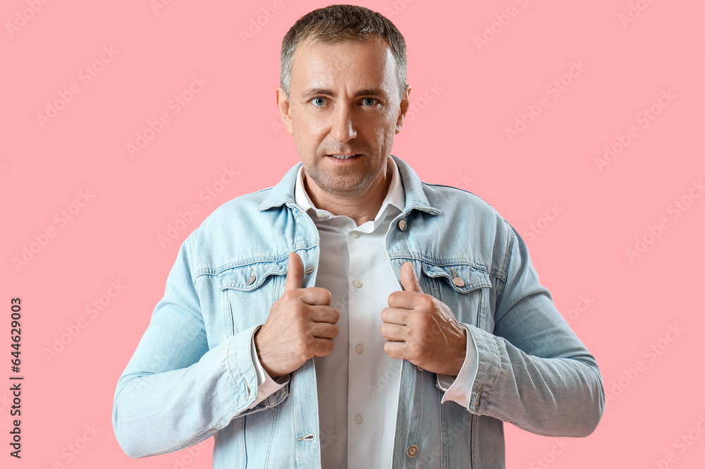 Portrait of confident mature man in denim jacket on pink background