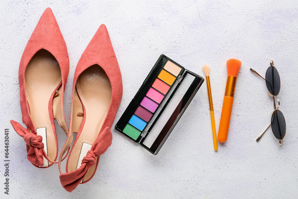 Stylish female shoes, eyeshadows, makeup brushes and sunglasses on light background