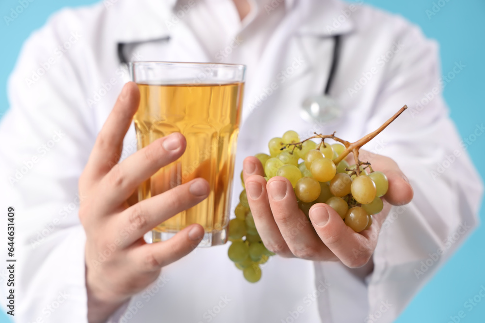 Male doctor with glass of juice and grape on blue background, closeup