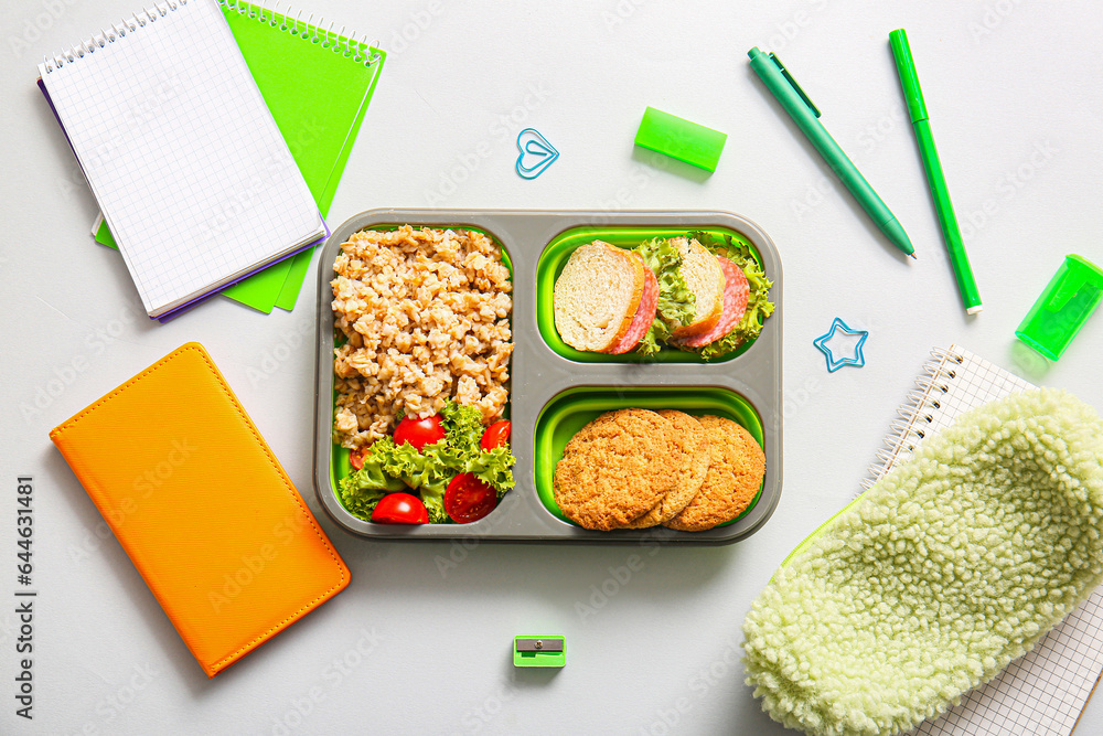 Lunchbox with delicious food and different stationery on white background