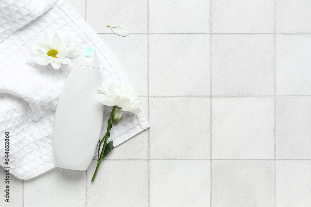 Composition with bottle of cosmetic product, towel and chamomile flowers on light tile background