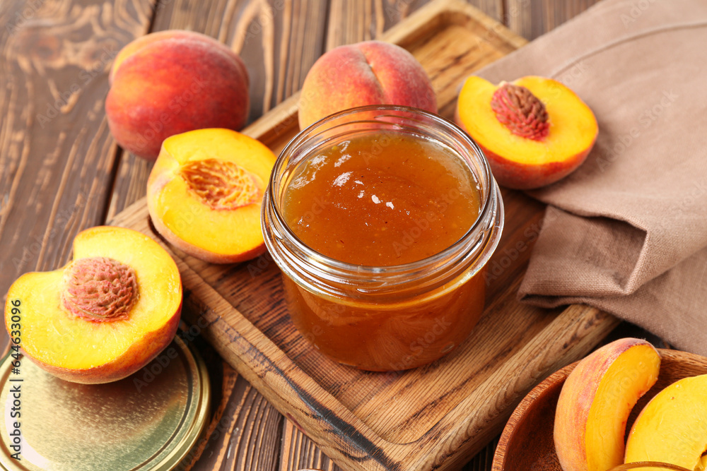 Cutting board with jar of sweet peach jam and fresh fruits on wooden background, closeup