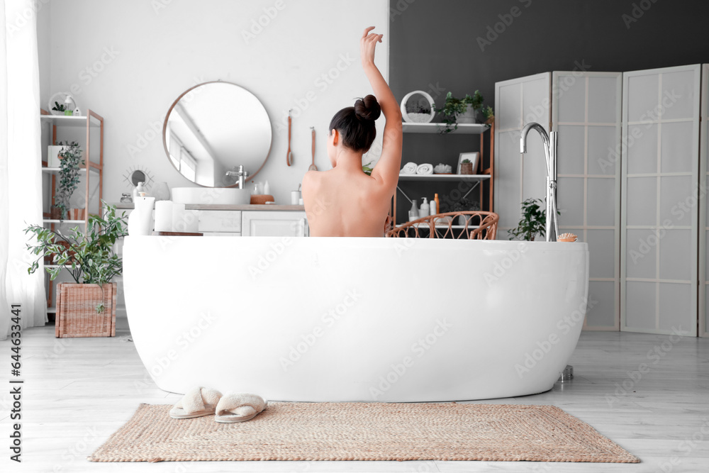 Young woman taking bath at home, back view