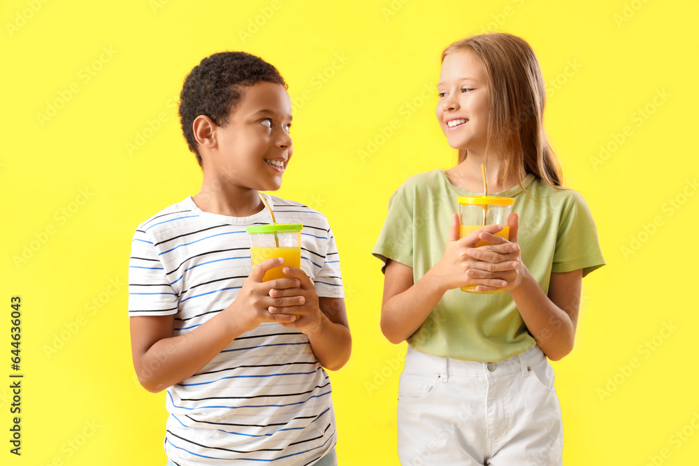 Little children with cups of fresh citrus juice on yellow background