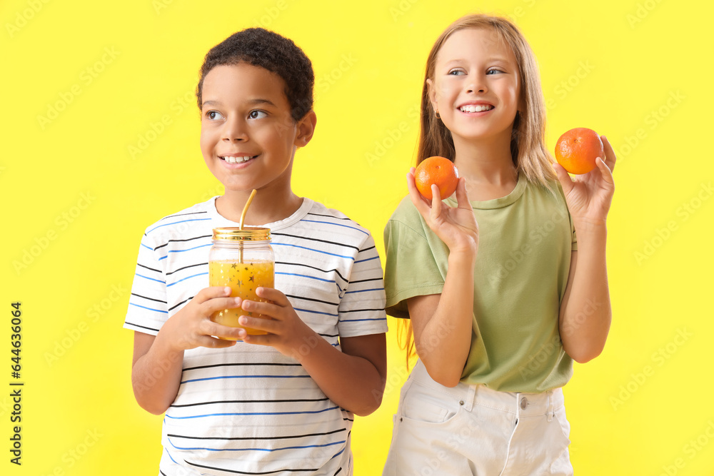 Little children with fresh tangerines and cup of juice on yellow background