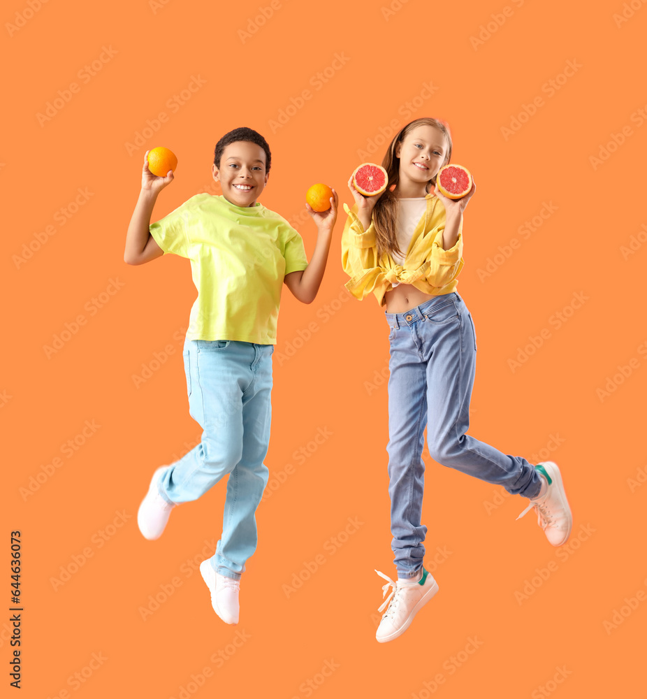 Little children with fresh citruses jumping on orange background