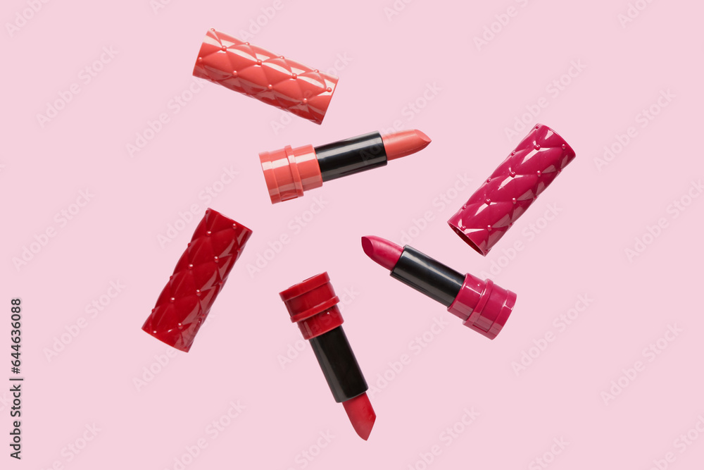 Different lipsticks flying on pink background