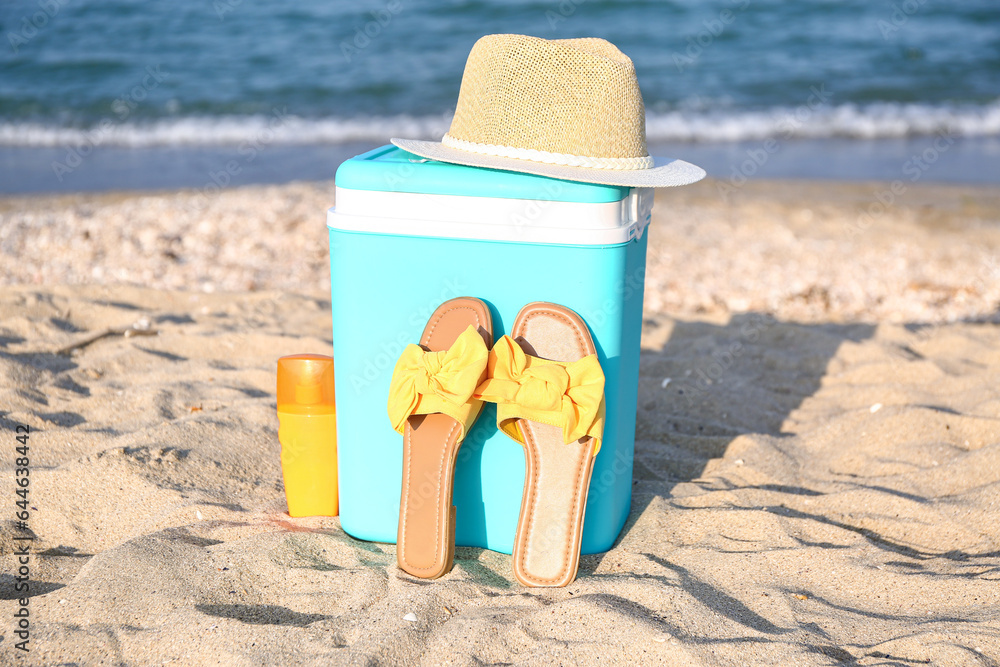 Beach cooler, stylish sandals, hat and sunscreen on sand