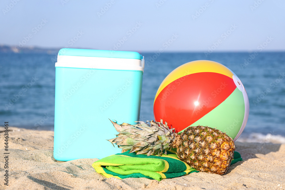 Beach cooler, inflatable ball, towel and pineapple on sand