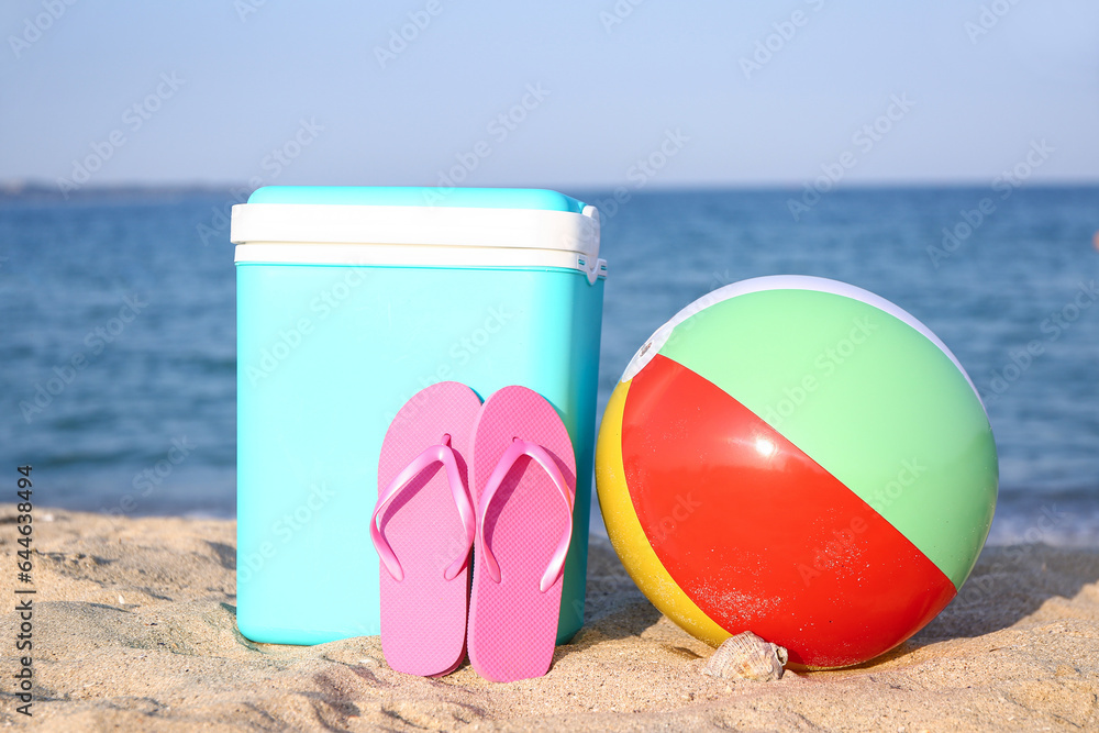 Beach cooler, inflatable ball and flip-flops on sand