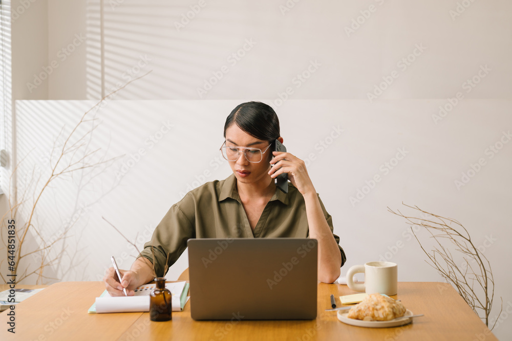 Asian businessperson is busy working, talking on the phone and taking notes in a notebook on a work 