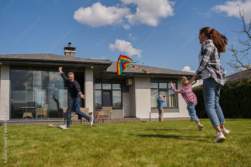 Happy family of mother, father and daughter playing with rainbow kite at summer