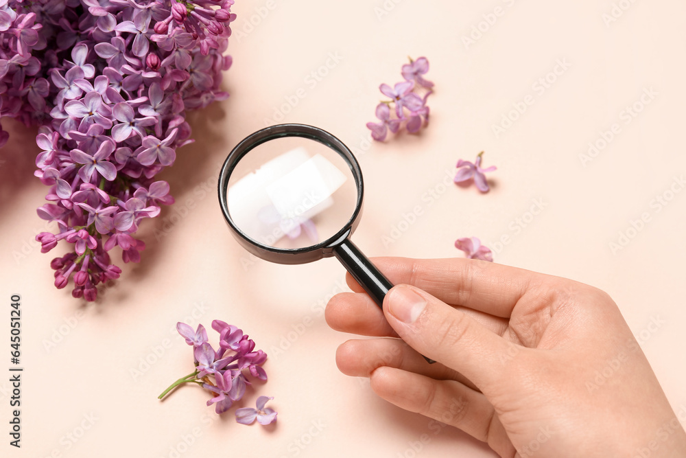 Female hand with magnifier and beautiful lilac flowers on pale pink background