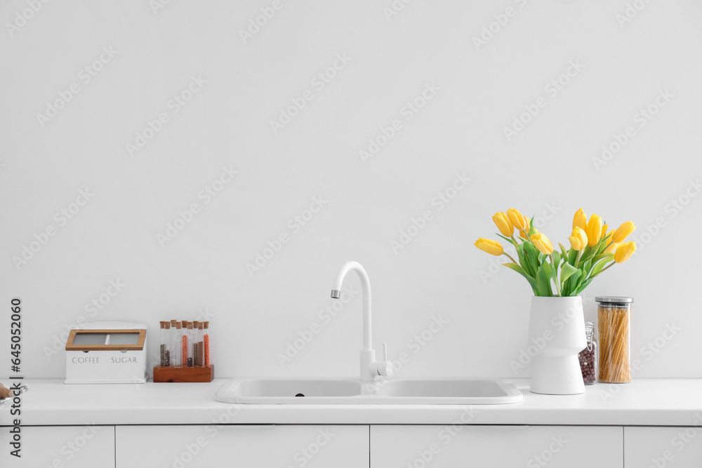 Vase with yellow tulip flowers on countertop near kitchen sink