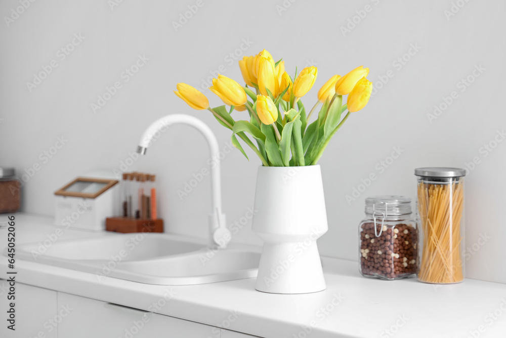 Vase with yellow tulip flowers on countertop near kitchen sink