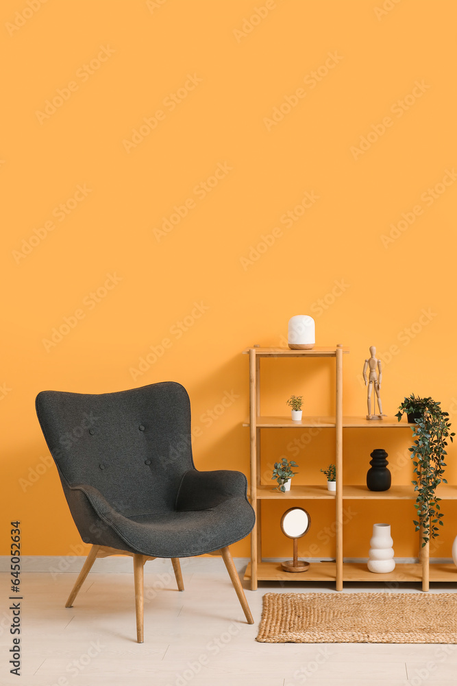 Dark grey armchair with shelving unit, houseplants and rug near orange wall