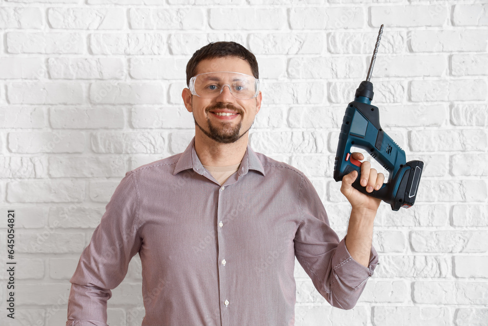 Male builder with drill near white brick wall