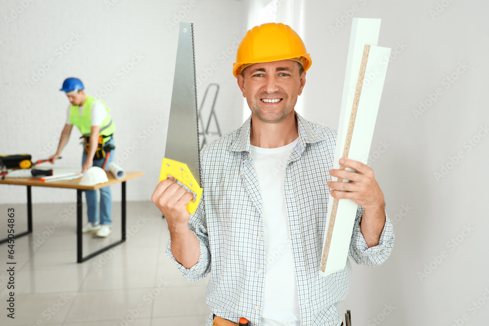 Mature builder with handsaw and wooden planks in room