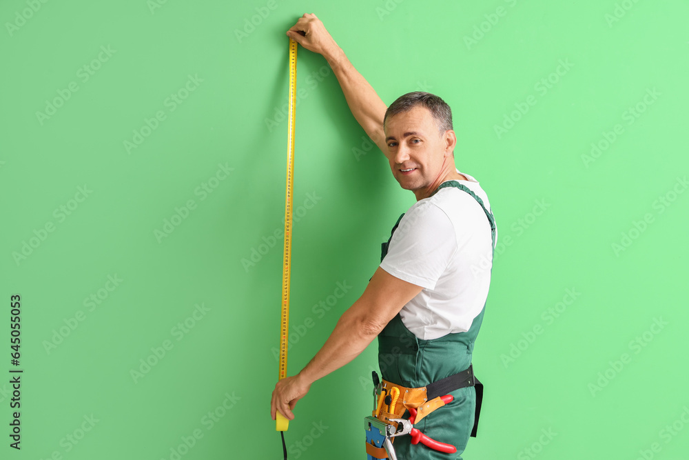 Mature builder with tape measure on green background