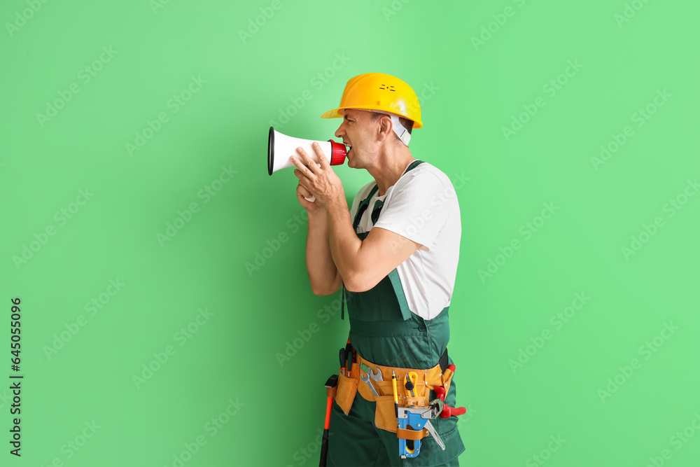 Mature builder shouting into megaphone on green background