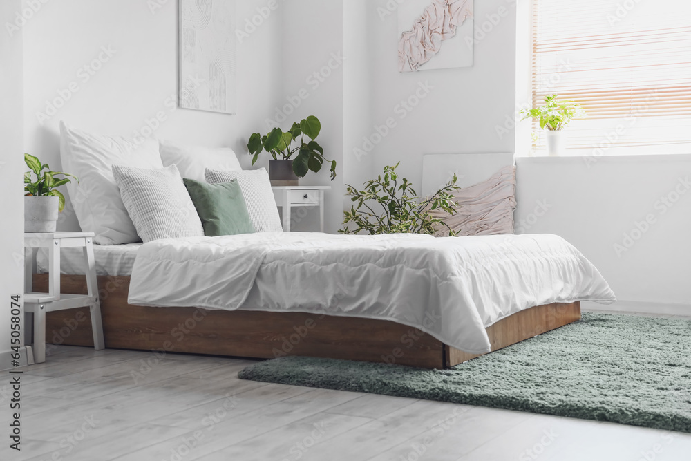 Cozy bed with white blanket and pillows in interior of light bedroom