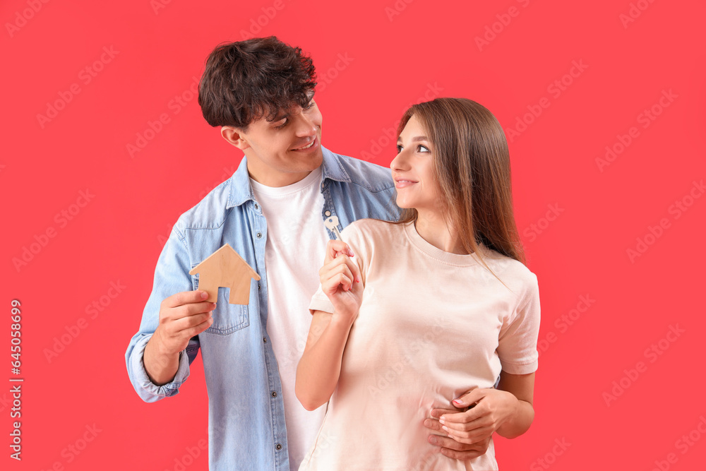 Young couple with key and house figure on red background